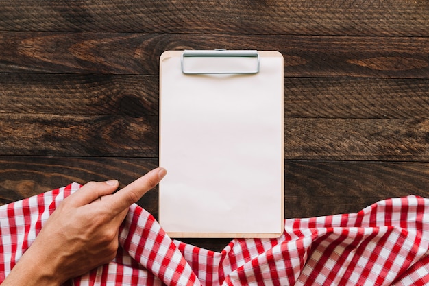 Crop hand pointing at clipboard near napkin