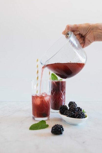 Crop hand pouring berry beverage into glass