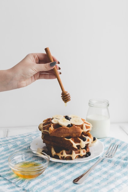 Crop hand pouring honey on waffles