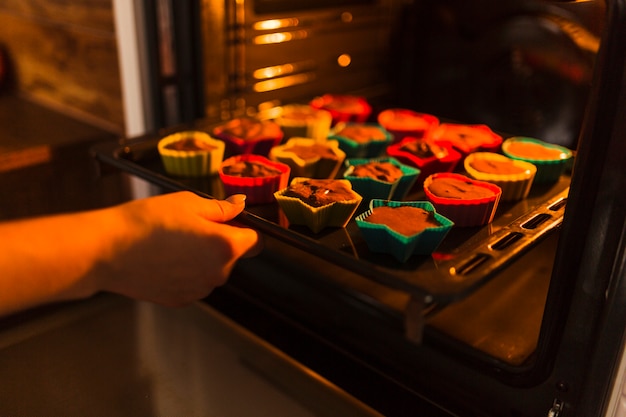 Crop hand putting cupcakes into oven