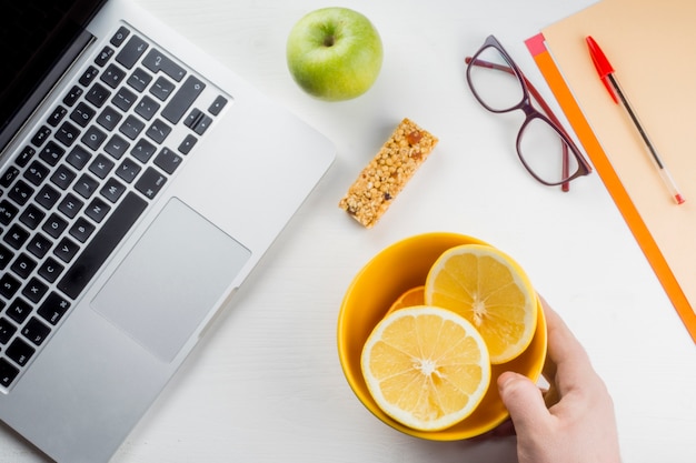 Crop hand putting orange near laptop