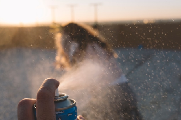 Crop hand spraying foam on blurred girl