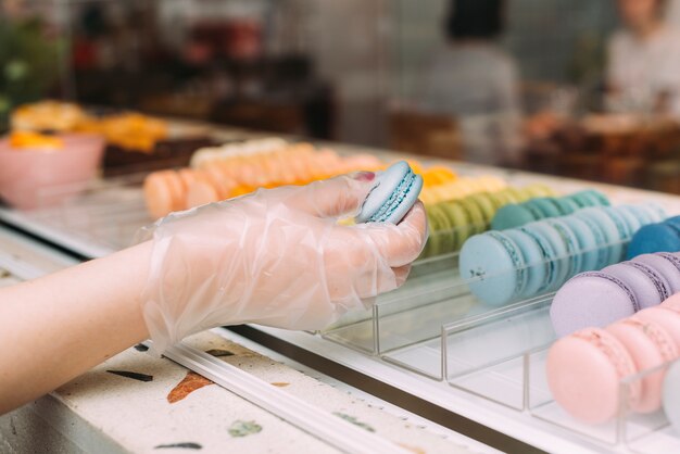 Crop hand taking macaroons from display case