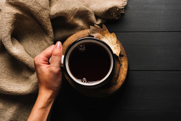 Crop hand with beverage near leaf and fabric