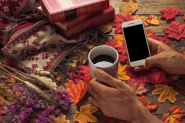 Crop hand with coffee and smartphone near autumn composition