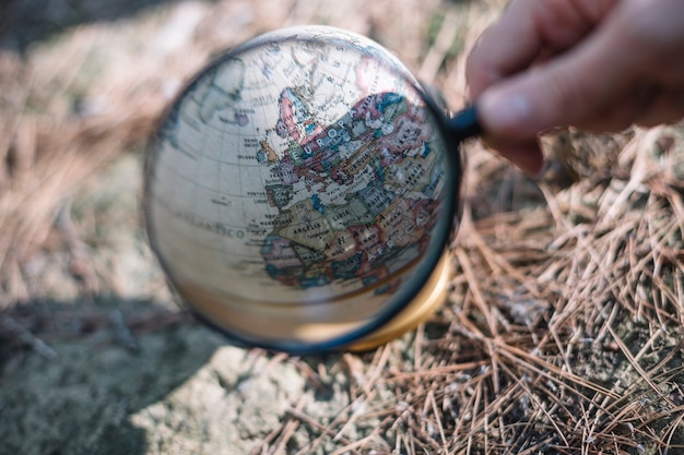 Crop hand with magnifying glass near globe
