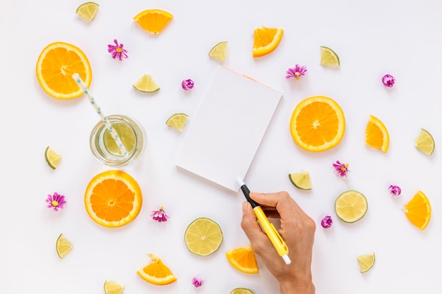 Crop hand writing near fruits and drink