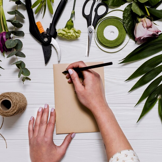 Crop hand writing on table with florist equipment