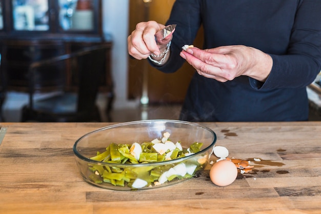 Crop hands of aged woman cutting eggs in kitchen