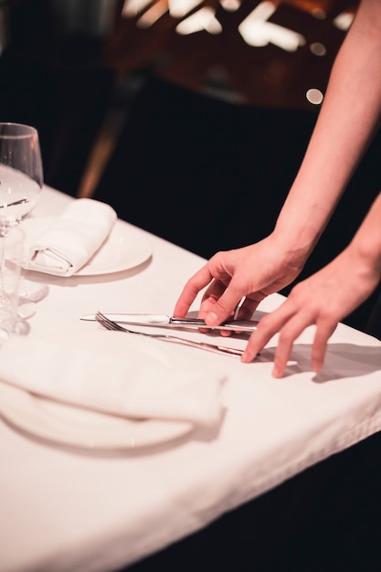 Crop hands arranging cutlery on table