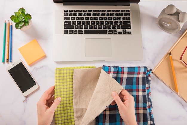 Crop hands choosing cloth near laptop