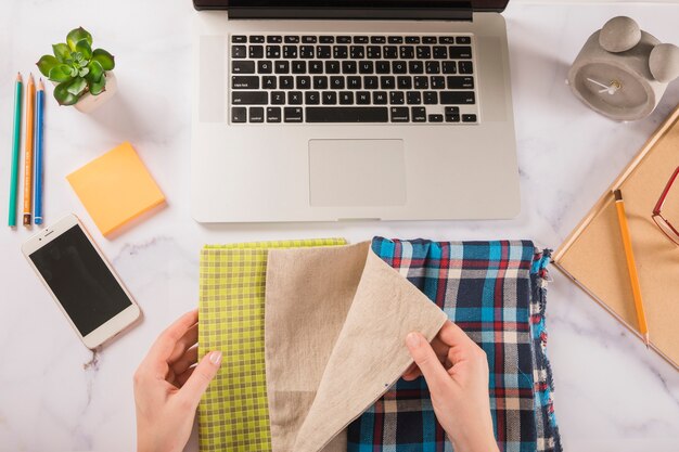 Crop hands choosing cloth near laptop