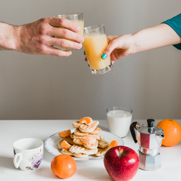 Crop hands clinking glasses with juice