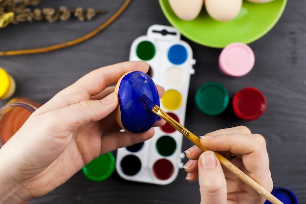 Crop hands coloring egg in blue