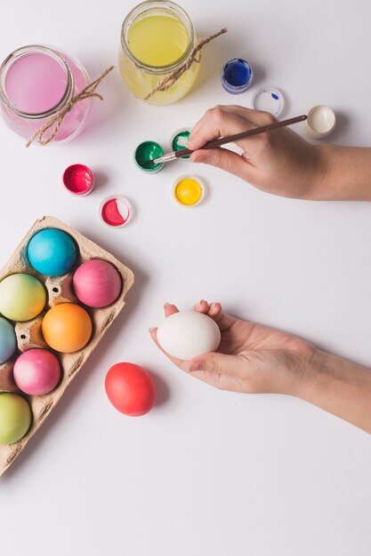 Crop hands coloring egg with green