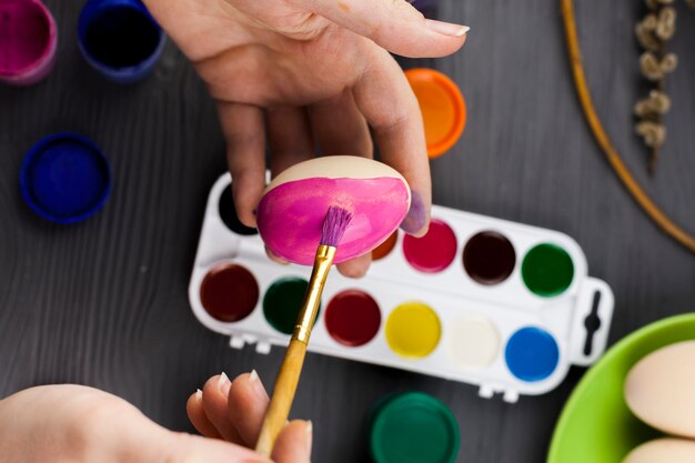 Crop hands coloring eggs in pink