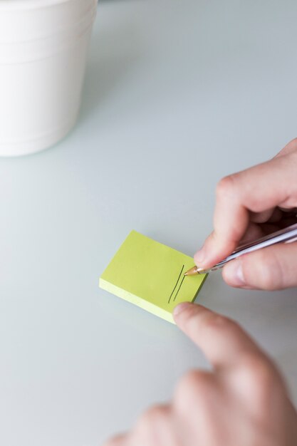 Crop hands drawing lines on sticky note