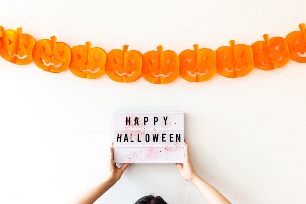 Foto gratuita ritaglia le mani che tengono il bordo con la scrittura vicino alla ghirlanda di halloween