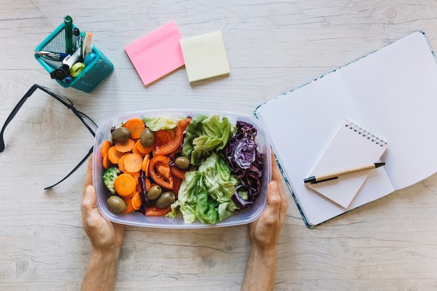 Crop hands holding box with salad over table