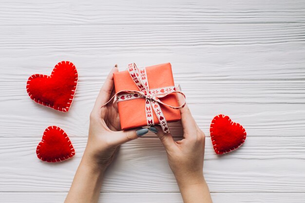 Crop hands holding gift box near hearts