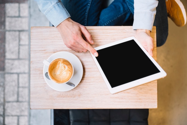 Crop hands holding tablet with coffee nearby