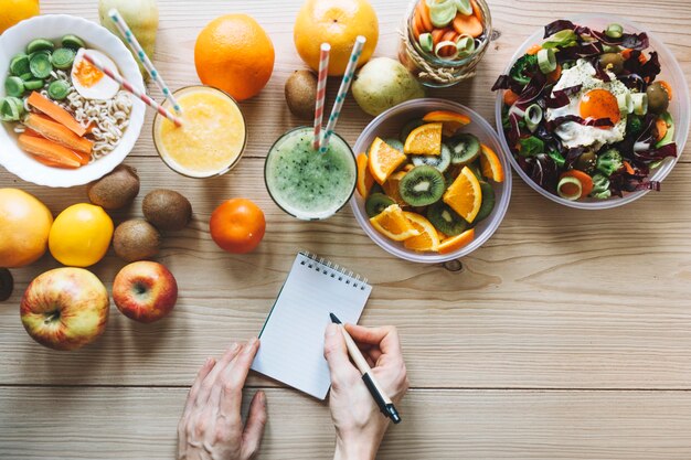 Crop hands making notes near healthy food