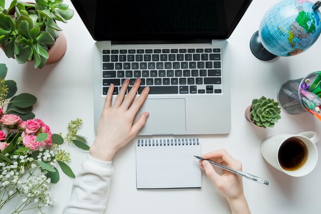 Crop hands making notes and using laptop