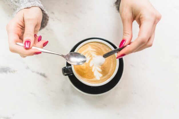 作物の手はカプチーノカップに砂糖を注ぐ