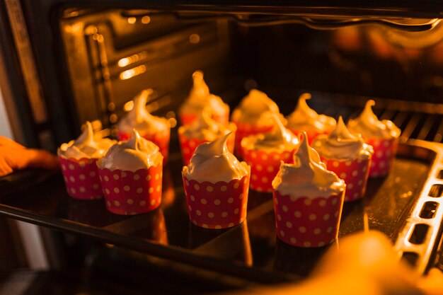 Crop hands putting cupcakes into oven