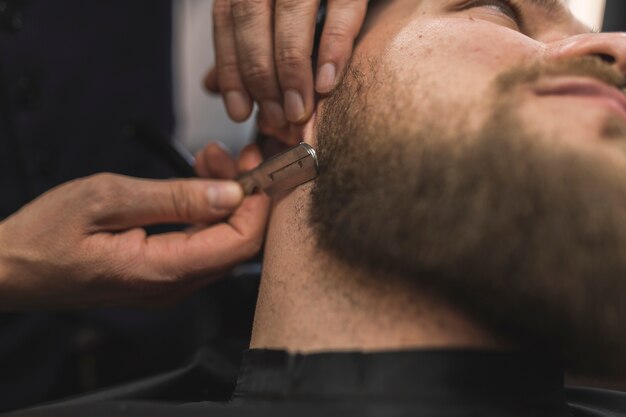 Crop hands shaving neck of customer