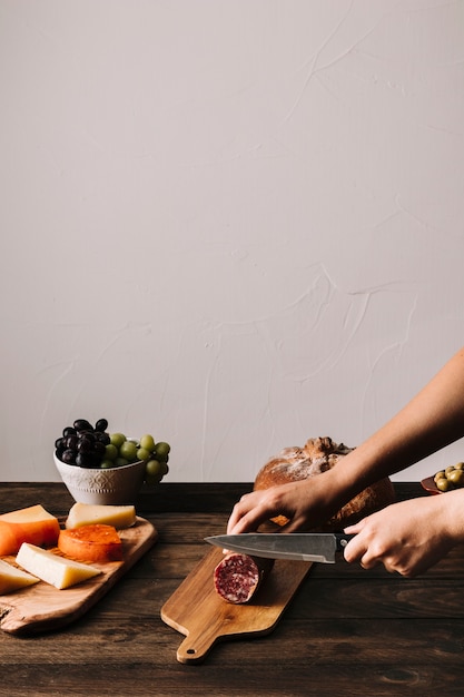 Crop hands slicing sausage on board