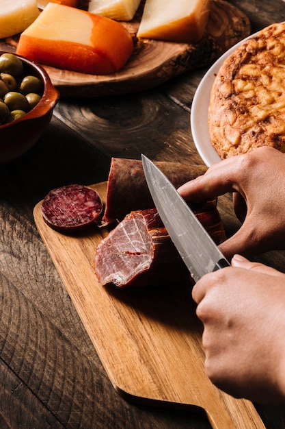 Foto gratuita ritaglia le mani affettando la carne affumicata vicino al cibo