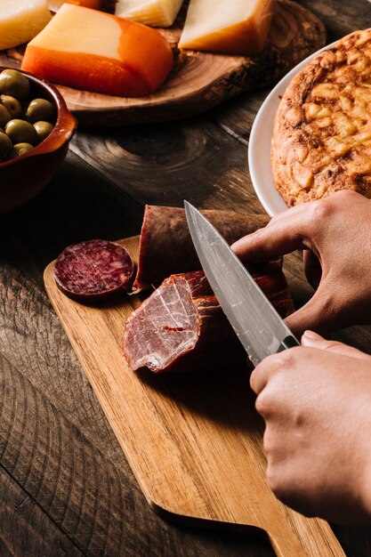 Crop hands slicing smoked meat near food