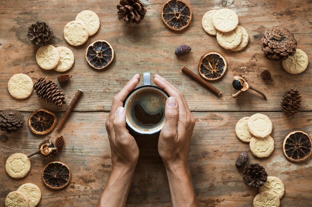 Crop hands warming near cup of coffee