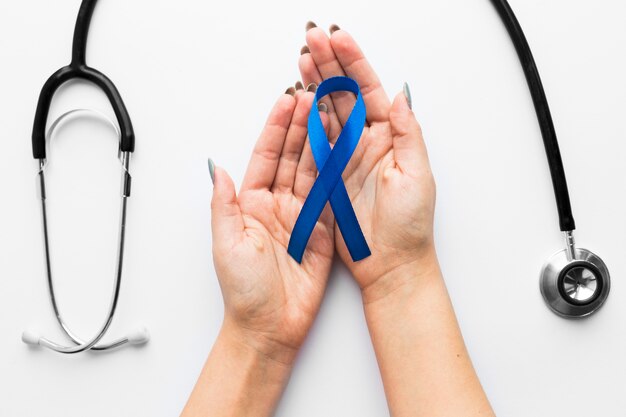 Crop hands with blue ribbon near stethoscope