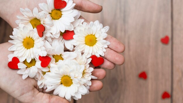 Crop hands with pile of flowers and hearts