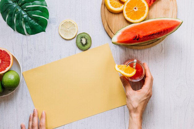 Crop hands with smoothie near orange paper and fruits