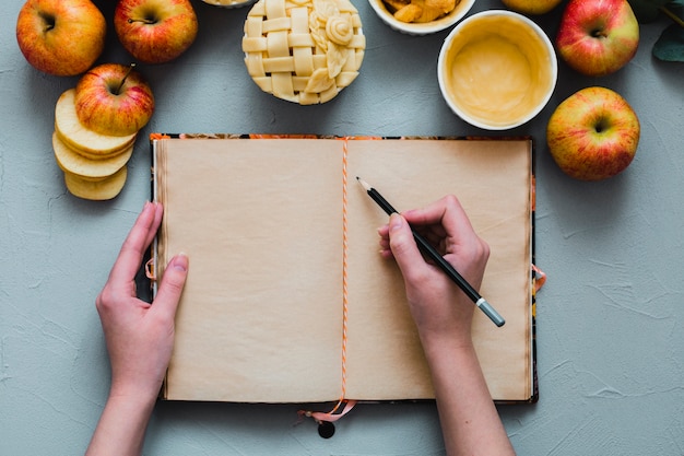 Foto gratuita ritaglia le mani scrivendo vicino a mele e torta