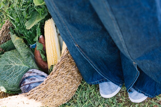 Crop legs near basket with vegetables