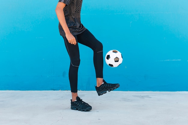 Crop legs of sportsman kicking soccer ball