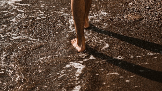 Ritagliare le gambe camminando vicino alle onde del mare