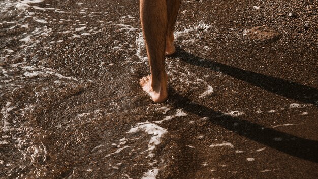 Crop legs walking near sea waves