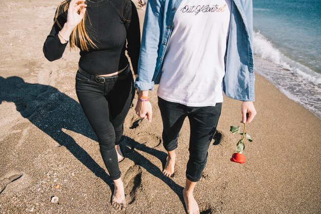 Crop loving people walking barefoot on beach