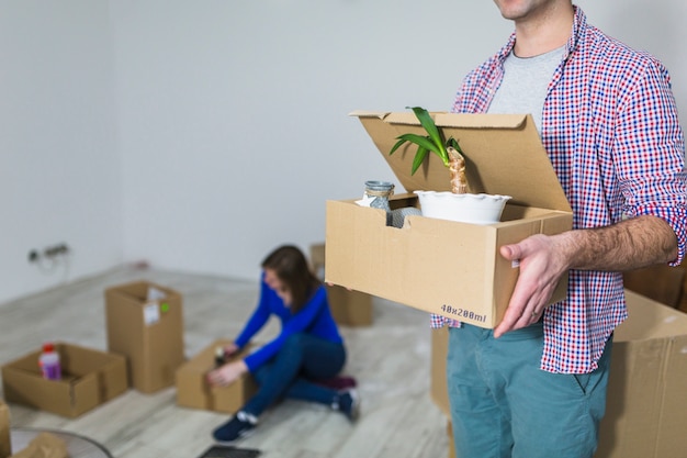 Crop man carrying box with plant