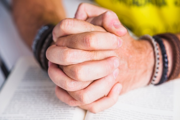 Crop man clasping hands on book