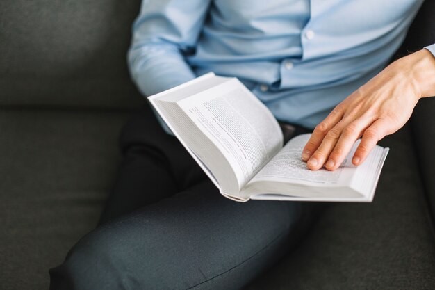 Crop man enjoying reading on couch