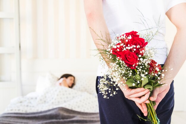 Crop man hiding flowers behind back