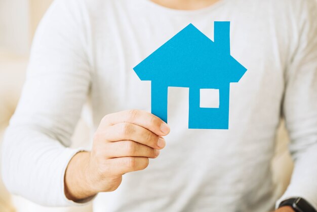 Crop man holding blue paper house