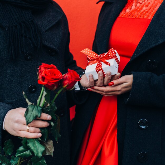 Crop man presenting flowers and box