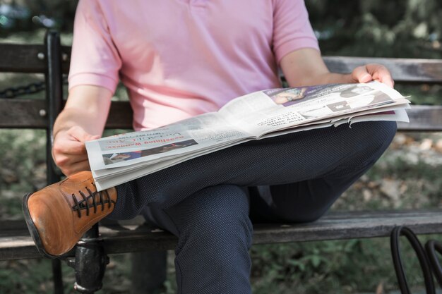 Crop man reading newspaper on bench